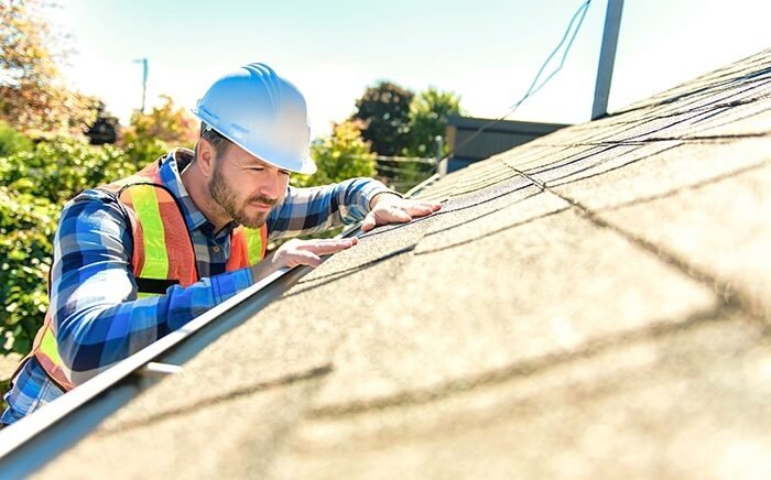 A man with hard hat standing on steps inspecting house roof for roof inspections