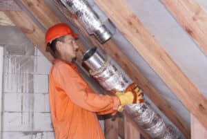 Attic Ventilation. Worker In The Attic Connects Metal Air Ducts.