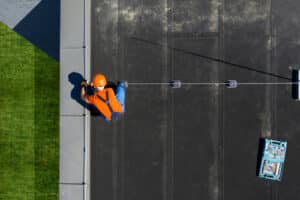 Caucasian Technician Wearing Orange Uniform and Hard Hat Installing commercial roofing Protection System Rod on Top of Commercial Building