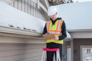 Home Prevention inspector on a ladder while writing on a clipboard during winter