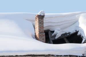 The roof collapsed under the weight of snow. Damaged falling roof and chimney on sunny day with clear blue sky