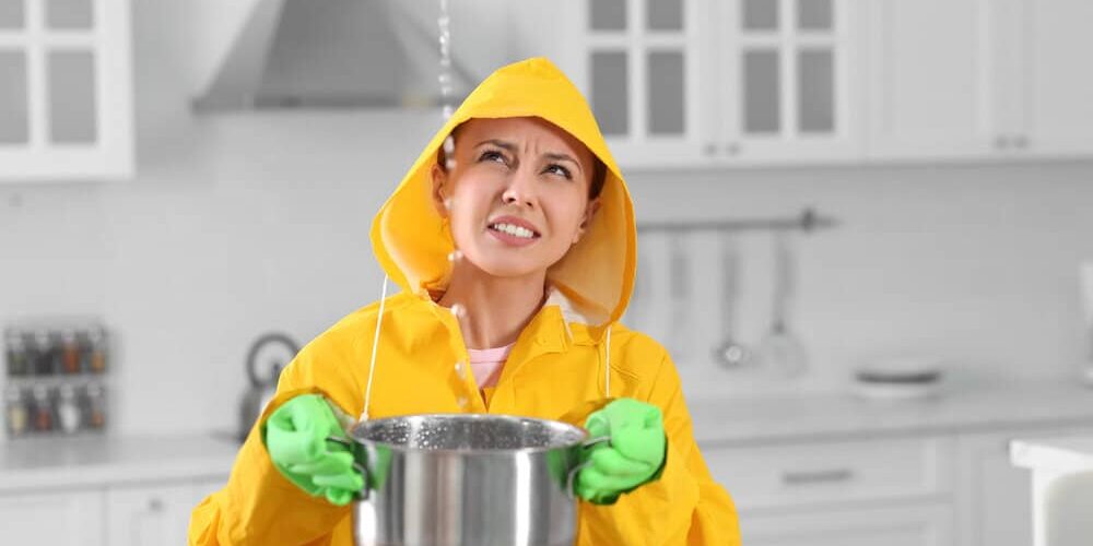 Roof Leaks. Young Woman In Raincoat Collecting Leaking Water From Ceiling. Roof Leaks. Young Woman In Raincoat Collecting Leaking Water From Ceiling.