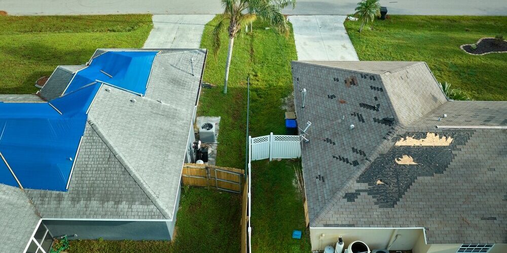 Roofing Contractors. Aerial View Of Damaged In Hurricane House Roof Covered. Roofing Contractors. Aerial View Of Damaged In Hurricane House Roof Covered.