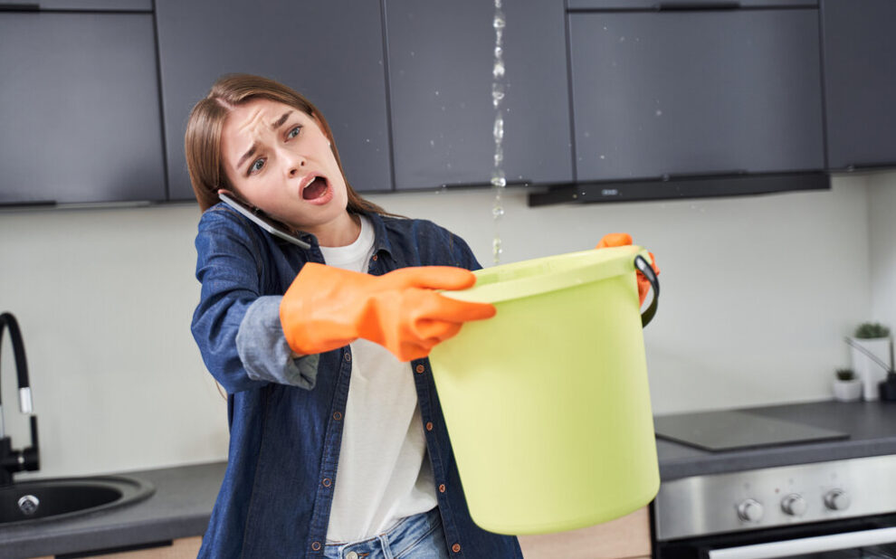 Roof Leak Repair. Woman holding bucket to catch water leaking from roof.