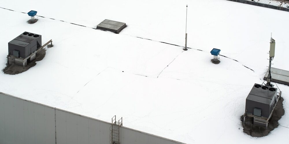 shutterstock_2087866948 (1) Commercial Roofing. Roof of a commercial building with a external units of the commercial air conditioning and ventilation systems, cellular antenna and lightning rod. Winter photo.
