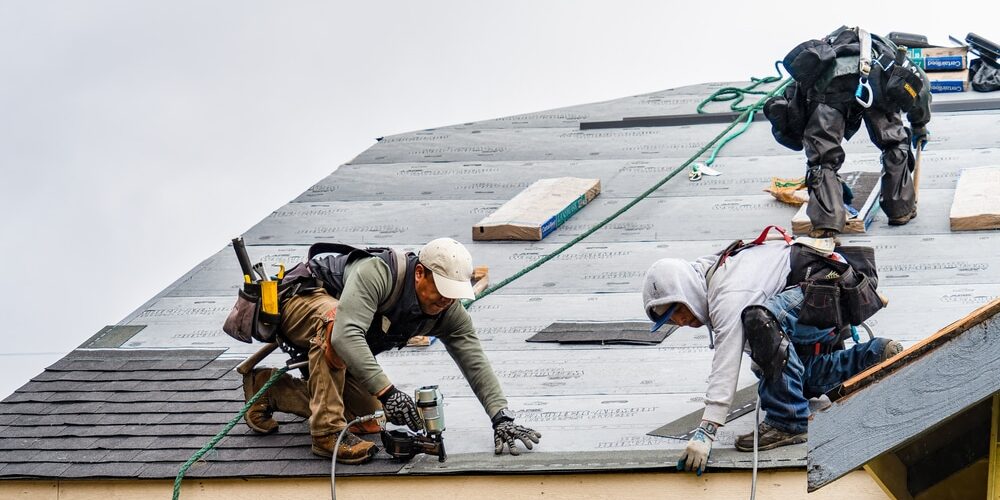 shutterstock_1948986700 (1) Winter Roof Repairs. Professionals repairing damage to roof from winter storm.
