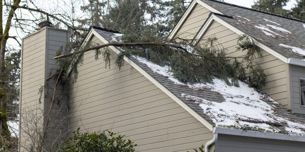 shutterstock_2415408051 (1) Roofing Contractors. Fallen tree branches on the roof of a residential building after severe winter snow storm.