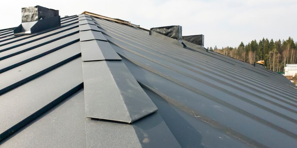 shutterstock_1357100900 (1) Metal Roofing System. close up view of grey folding roof and chimney on waterproofing layer of house under construction.