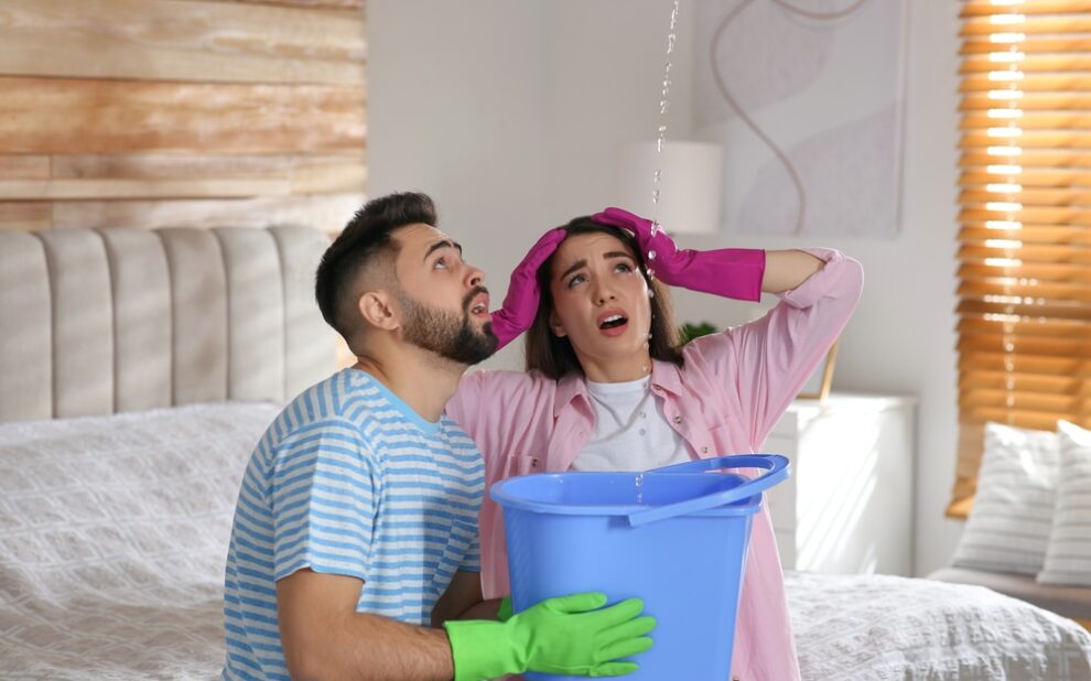 Leak Investigation Services. Young couple collecting leaking water from ceiling in bedroom. Time to call roof repair service.