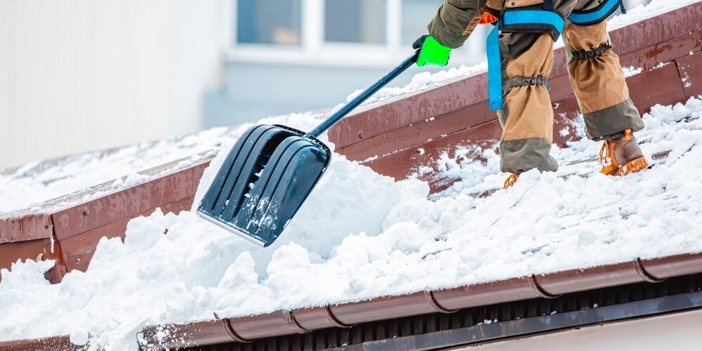 shutterstock_2559815385 (1) Snow and Ice Removal. worker removes snow from the building roof in winter.