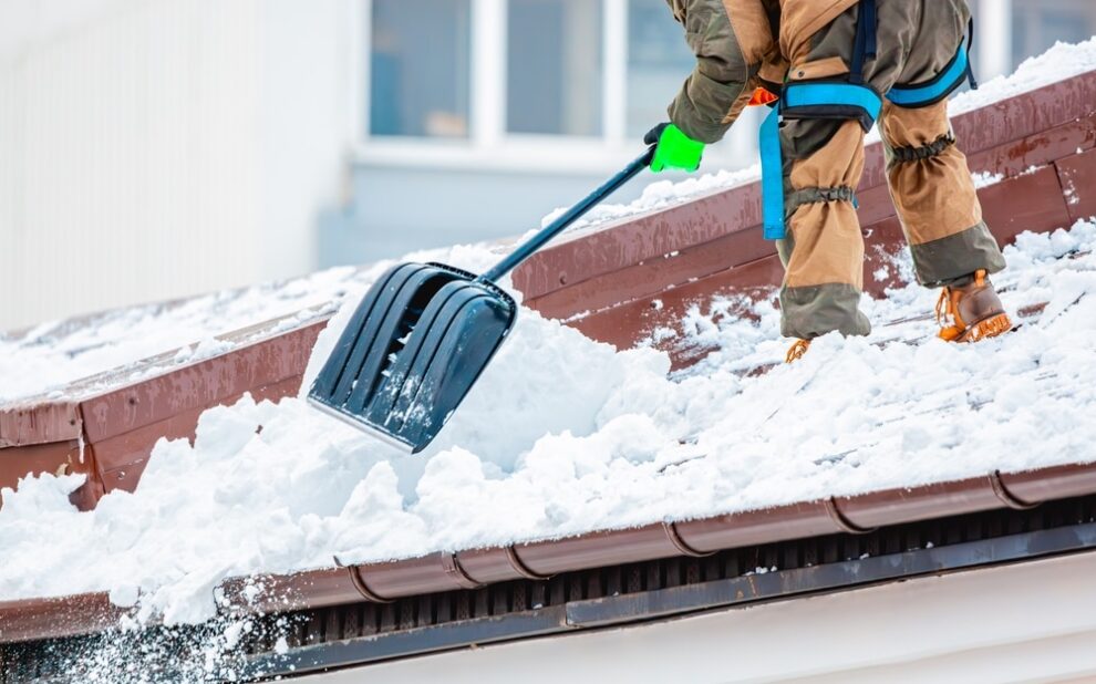 Snow and Ice Removal. worker removes snow from the building roof in winter.