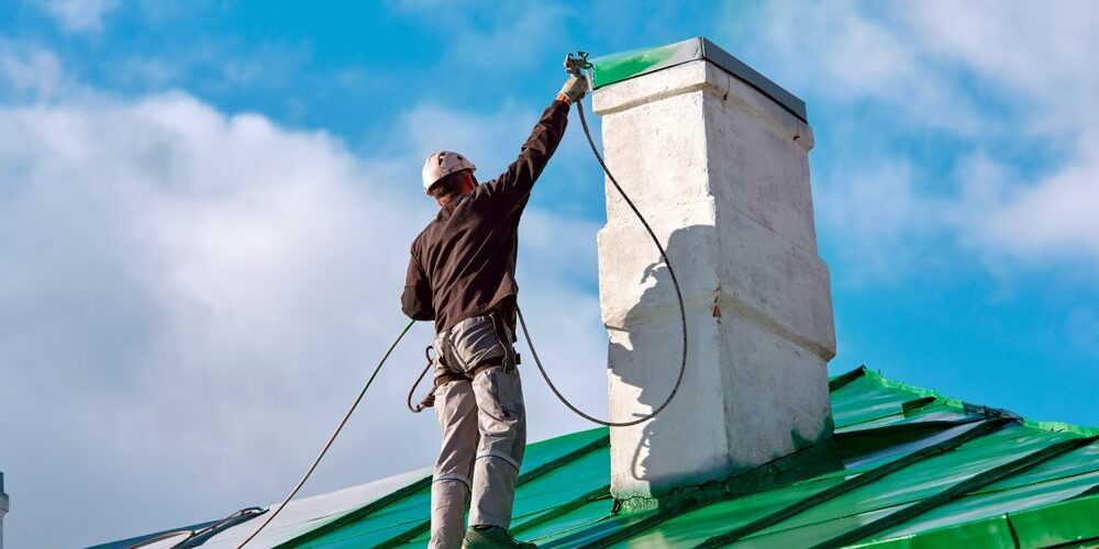 Worker,Of,Industrial,Alpinist,Services,Painting,Chimney,On,The,Roof Roof Coatings. Worker of Industrial Alpinist Services painting chimney on the roof with paint spray gun. Professional climber wearing uniform, helmet and using safety harness. Risky job. Extreme occupation.
