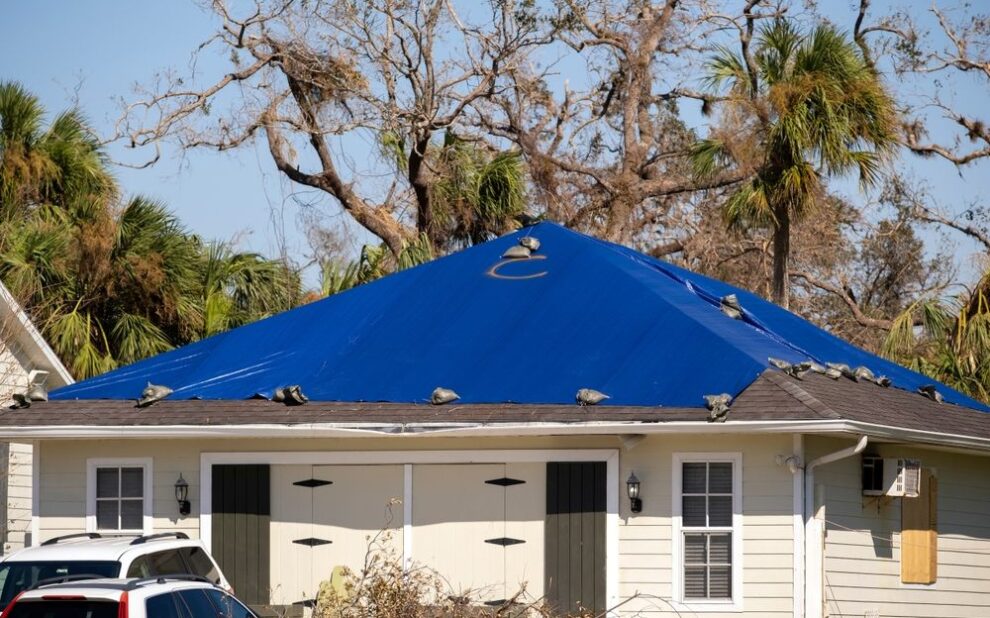 Insurance for Roof Repair. damaged house rooftop covered with protective plastic tarp against rain water leaking until replacement of asphalt shingles. Aftermath of natural disaster.