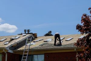 Residential Roofing. Roof repair, worker with replacing gray tiles shingles on house being applied.