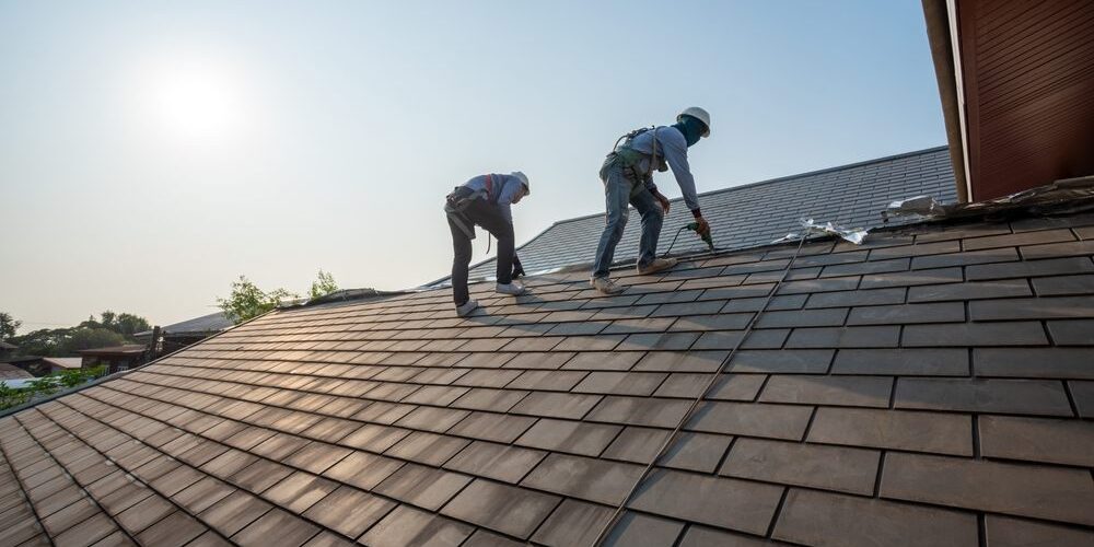 Roofer,Working,In,Special,Protective,Work,Wear,Gloves,,Using,Air Residential Roofing. Roofer working in special protective work wear gloves, using air or pneumatic nail gun repair and replace roofing tiles on top of the new roof under construction residential building.