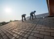 Residential Roofing. Roofer working in special protective work wear gloves, using air or pneumatic nail gun repair and replace roofing tiles on top of the new roof under construction residential building.