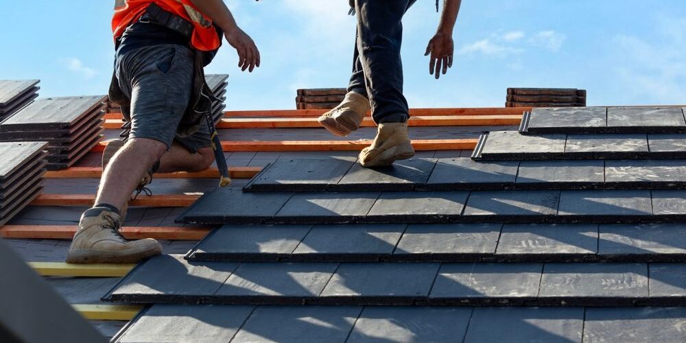 Roofers,Install,Slate,Tiles,On,A,Sunny,Day,At,A Why Is Godfrey Roofing Ottawa’s Premier Roof Contractor Since 1984? Roofers install slate tiles on a sunny day at a construction site in a suburban area.