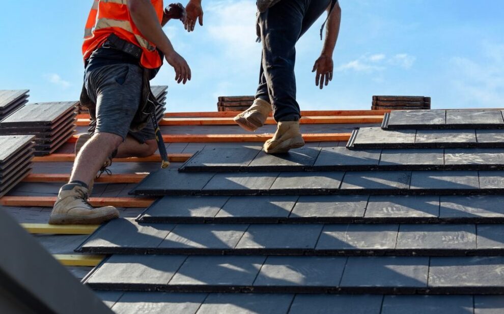 Why Is Godfrey Roofing Ottawa’s Premier Roof Contractor Since 1984? Roofers install slate tiles on a sunny day at a construction site in a suburban area.