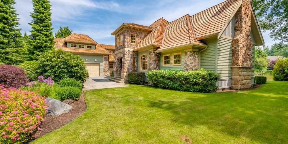 Large,Stately,Home,Exterior,With,Extensive,Stone,Cladding,Brick,Chimney Why Is Cedar Roof Replacement Popular in Ottawa? Large stately home exterior with extensive stone cladding brick chimney cedar shake roof on lush landscaping paved driveway blue sky estate house