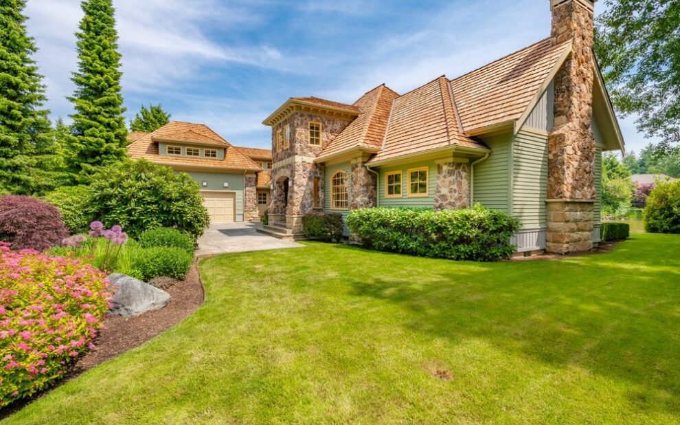Why Is Cedar Roof Replacement Popular in Ottawa? Large stately home exterior with extensive stone cladding brick chimney cedar shake roof on lush landscaping paved driveway blue sky estate house