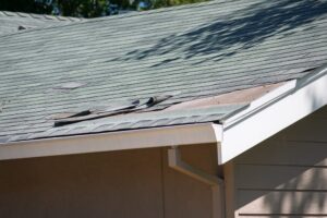 When Should Ottawa Homeowners Replace Shingle Roofs? Damaged asphalt shingles are visible on a residential roof, with several pieces curled and missing, revealing the wooden underlayment beneath.
