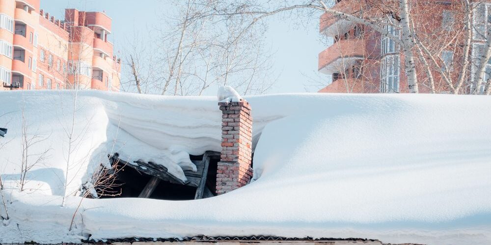 How Ottawa’s Harsh Winters Affect Your Roof and What To Do About It. The roof collapsed under the weight of snow. Damaged falling roof and chimney on sunny day with clear blue sky.
