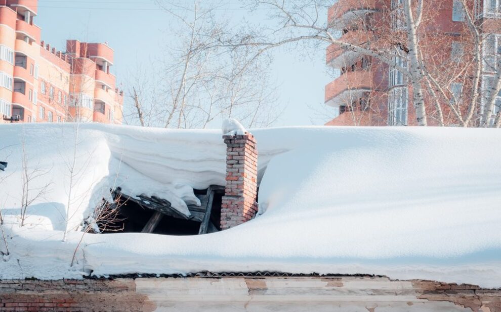 How Ottawa’s Harsh Winters Affect Your Roof and What To Do About It. The roof collapsed under the weight of snow. Damaged falling roof and chimney on sunny day with clear blue sky.