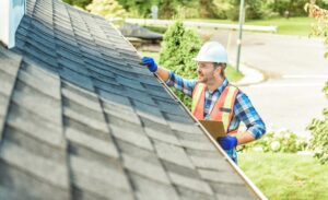 When to Schedule Professional Roof Inspections for Your Property? A man with hard hat standing on ladder inspecting house roof. On a sunny day.