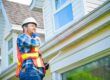 Why Seasonal Roof Inspections Are Critical Before Winter Hits. A man with hard hat standing on steps inspecting house roof.