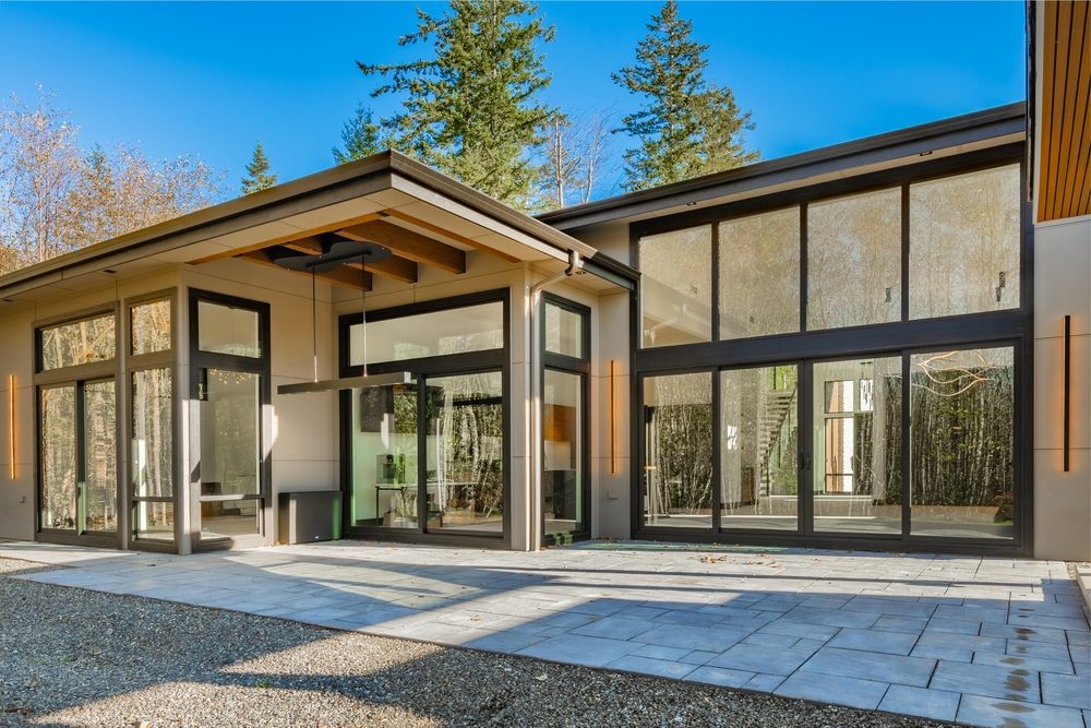 Residential Flat Roofs. Contemporary modern home exterior with black framed floor to ceiling windows cedar siding painted white brick walls glass and black garage doors elegant slim line exterior light fixtures and flat roof.