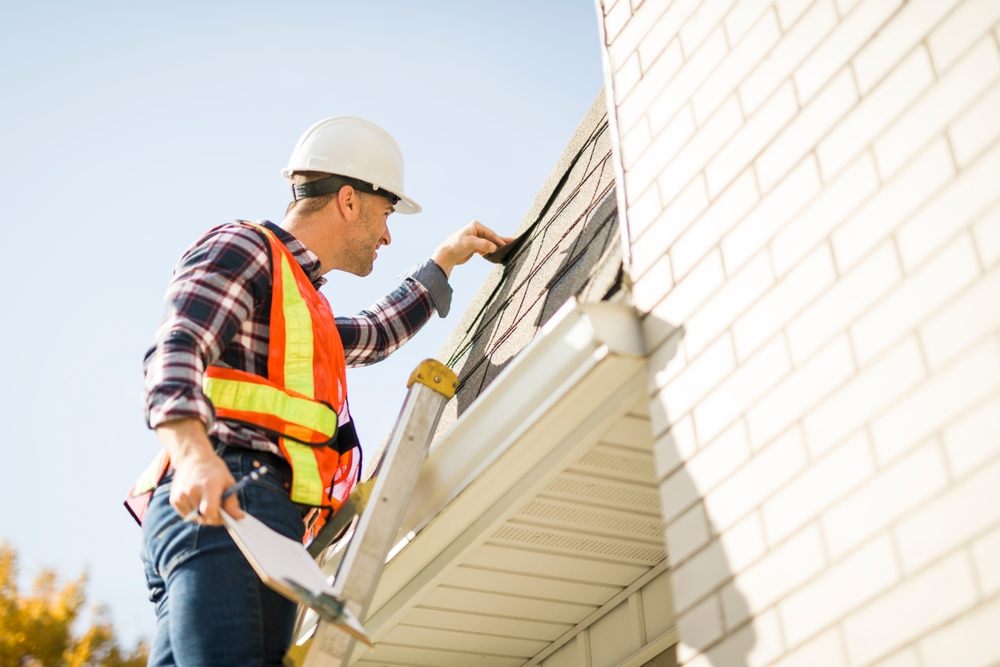 Why Seasonal Roof Inspections Are Important Before Winter Hits. A man with hard hat standing on steps inspecting house roof.