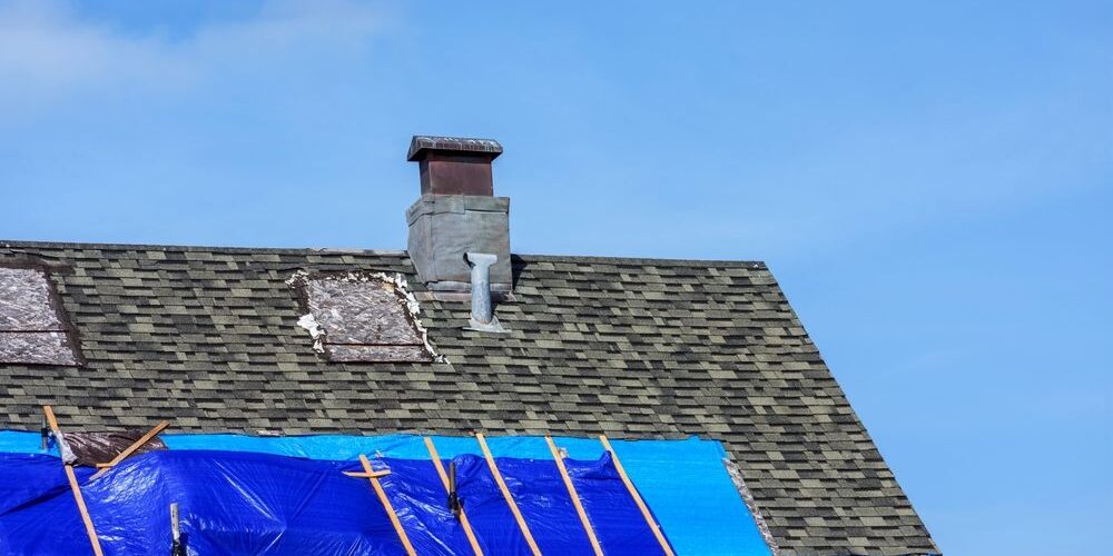 Roof,With,Damaged,Shingles,And,Blue,Tarp,Secured,By,Wooden Comprehensive Roof Repairs: How to Identify & Fix Common Roofing Issues. Roof with damaged shingles and blue tarp secured by wooden battens during repair.
