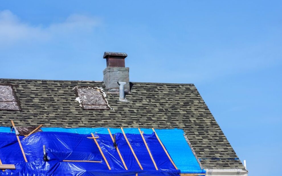 Comprehensive Roof Repairs: How to Identify & Fix Common Roofing Issues. Roof with damaged shingles and blue tarp secured by wooden battens during repair.