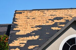 Spring Thaw & Your Roof: Why Melting Snow Can Lead to Critical Roof Repair. Wind-damaged house roof with missing asphalt shingles. Repair of the home rooftop concept.
