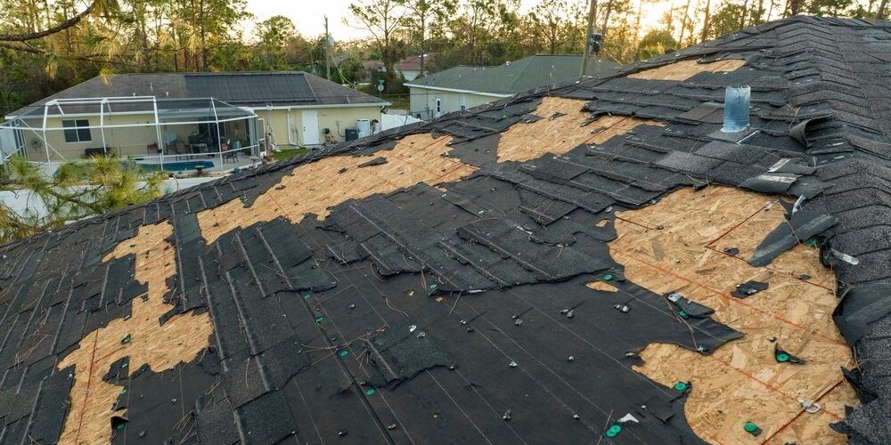 Spring Thaw & Your Roof: Why Melting Snow Can Lead to Critical Roof Repair. Ruined rooftop in need of repair. Wind damaged house roof with missing asphalt shingles.