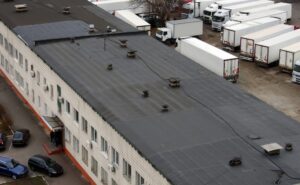 Commercial Roofing in Ottawa: A Strategic Guide for Property Resilience in 2026. View of the roof of a commercial building with passenger cars on one side of the building and semi-trailers on the other.