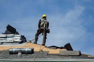 Finding the Best Roofing Contractors Near You: A Guide for Ottawa. Construction worker using pneumatic nailer and safety helmet applying roofing materials against a blue sky backdrop.