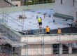 Plan a Commercial Roofing Project Timeline Without Disruption. Birdseye view of roofer waterproofing the flat roof of a commercial building.