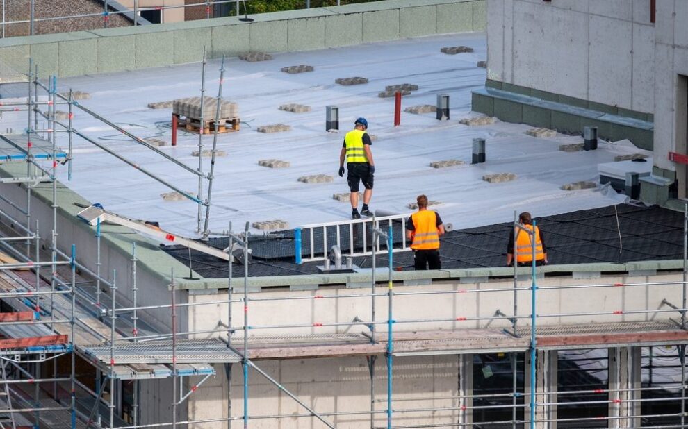 Plan a Commercial Roofing Project Timeline Without Disruption. Birdseye view of roofer waterproofing the flat roof of a commercial building.