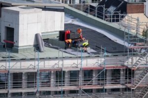 Plan a Commercial Roofing Project Timeline Without Disruption. Birdseye view of a roofer waterproofing the flat roof of a commercial building.