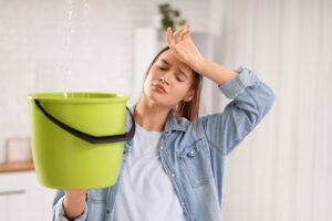 Compare Roofing Materials for Homes in Ottawa: Durability, Cost, & Aesthetics. Tired young woman placing green bucket under water dripping from ceiling at home.
