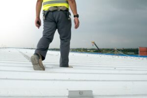 The Step-by-Step Process Commercial Roof Contractors Use for Large-Scale Roof Replacement. A roofing engineer wears a safety uniform, inspects metal roofing work for a roof industrial concept with copy space.