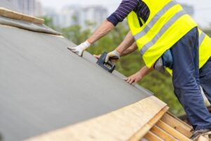 Choose the Best Residential Roofing for Your Ottawa Home Renovation. A man is working with a stapler and a special waterproof bitumen membrane. Mature and professional contractor in protective uniform standing on the rooftop of a new modern building construction.