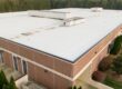 The Step-by-Step Process Commercial Roof Contractors Use for Large-Scale Roof Replacement. Professional aerial perspective of a modern commercial flat roof featuring a white TPO single-ply membrane installation. The image highlights the technical details of the roofing system, including the reflective surface designed for energy efficiency and UV resistance. The shot captures the symmetrical layout of the membrane sheets and the precision of the heat-welded seams, making it ideal for construction industry professionals, roofing contractors, and building inspectors. This high-resolution drone view emphasizes the scale and cleanliness of modern industrial infrastructure and sustainable building practices in 2026.